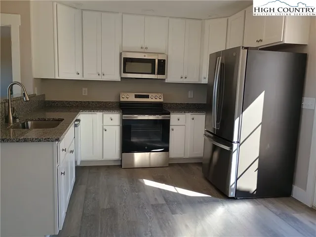 a kitchen with granite countertop a refrigerator stove and sink with wooden floor