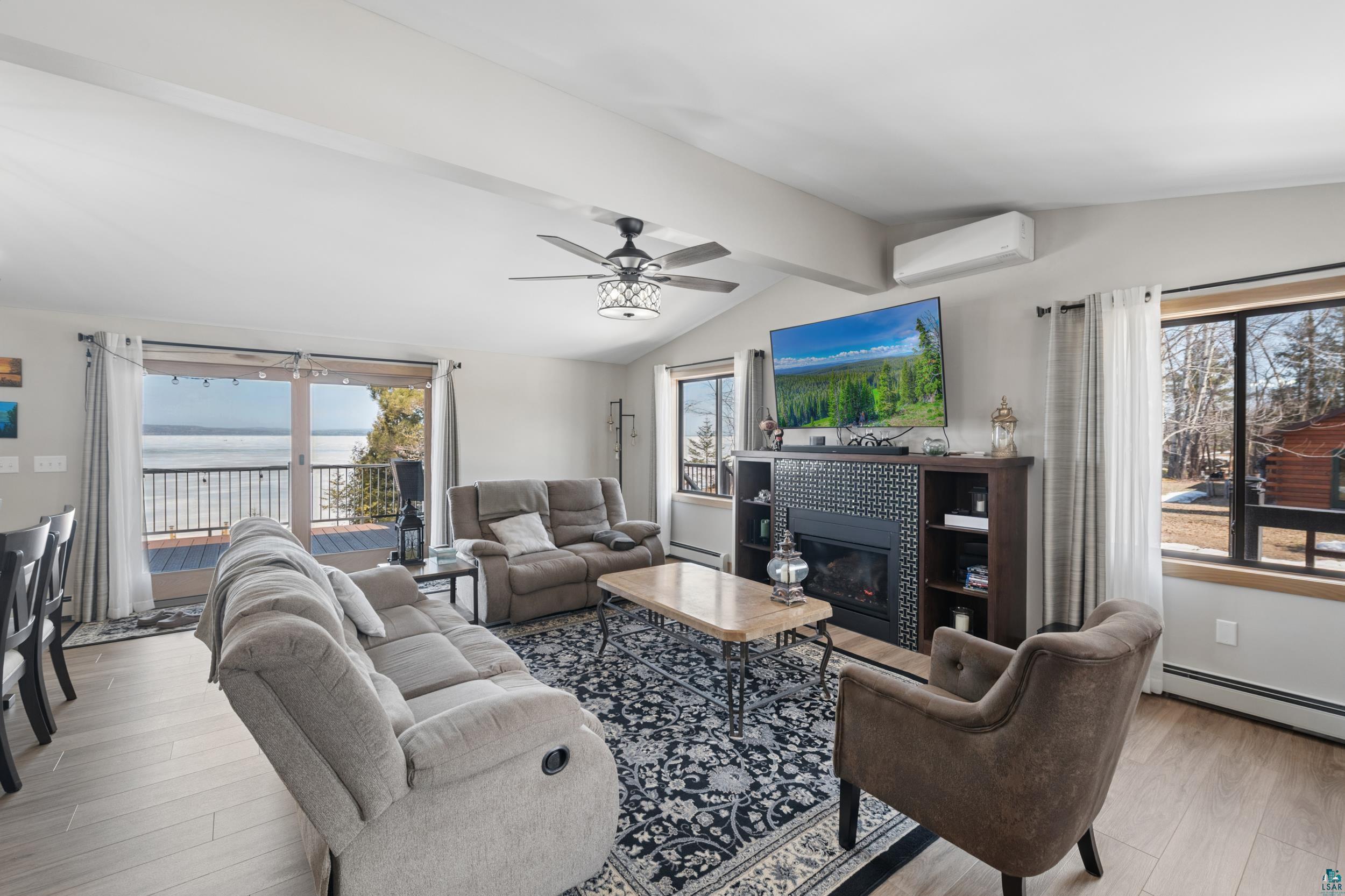 3903 Lake Park Road Ashland, WI 54806 - Photo 15 of 37 Living area featuring wood finished floors, vaulted ceiling with beams, a ceiling fan, a tile fireplace, and a baseboard radiator