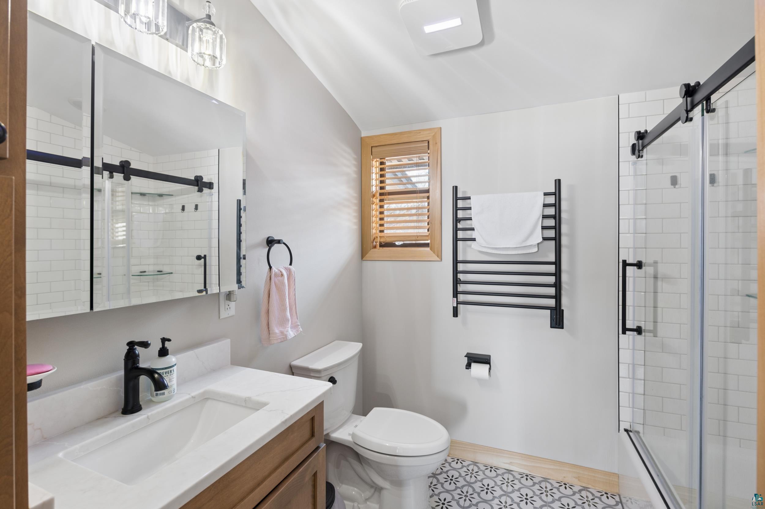 3903 Lake Park Road Ashland, WI 54806 - Photo 25 of 37 Bathroom featuring radiator, vanity, a towel warming rack, vaulted ceiling, and shower / bath combination with glass door
