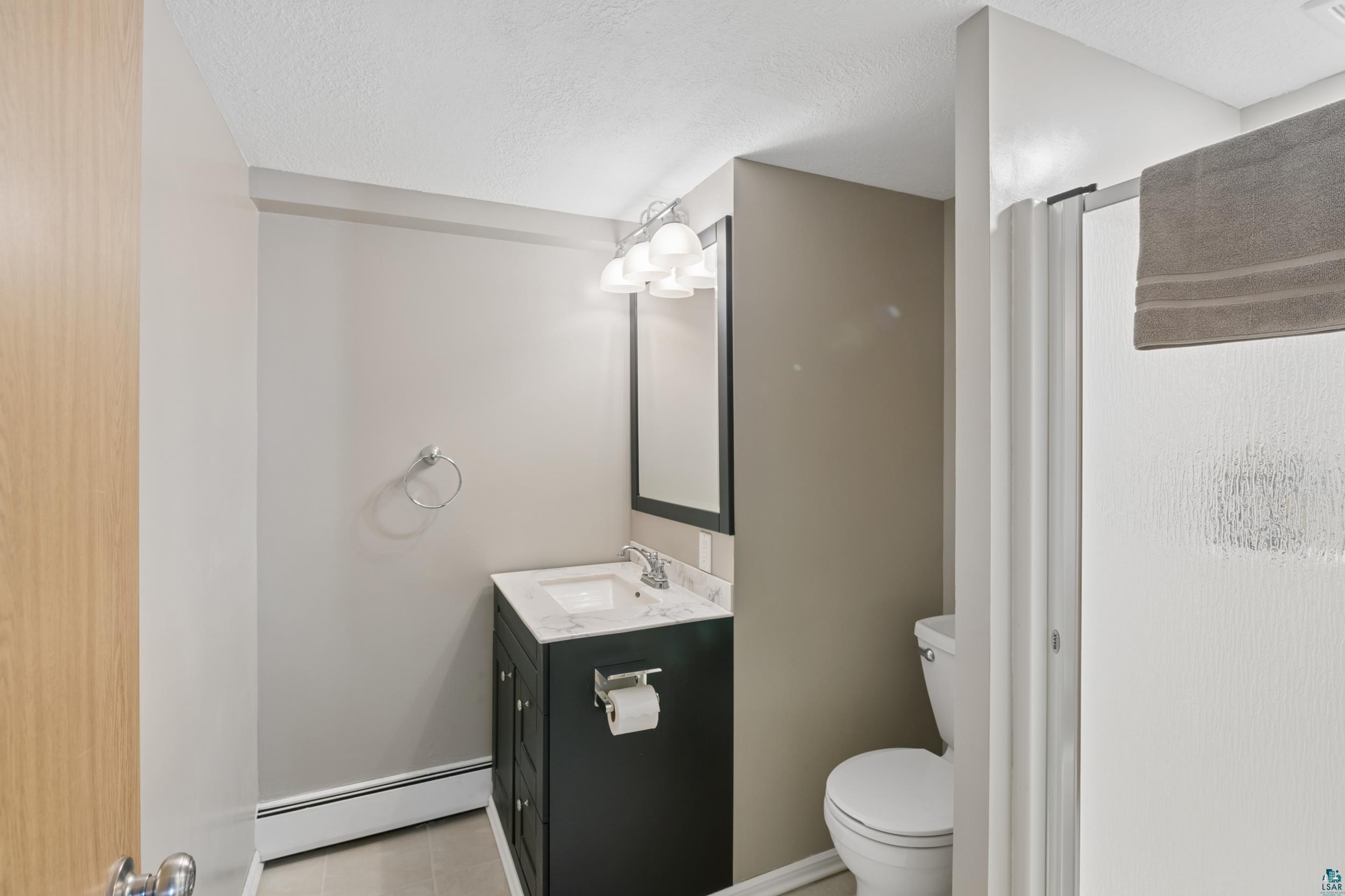 3903 Lake Park Road Ashland, WI 54806 - Photo 27 of 37 Full bath with vanity, a baseboard heating unit, a textured ceiling, and a stall shower