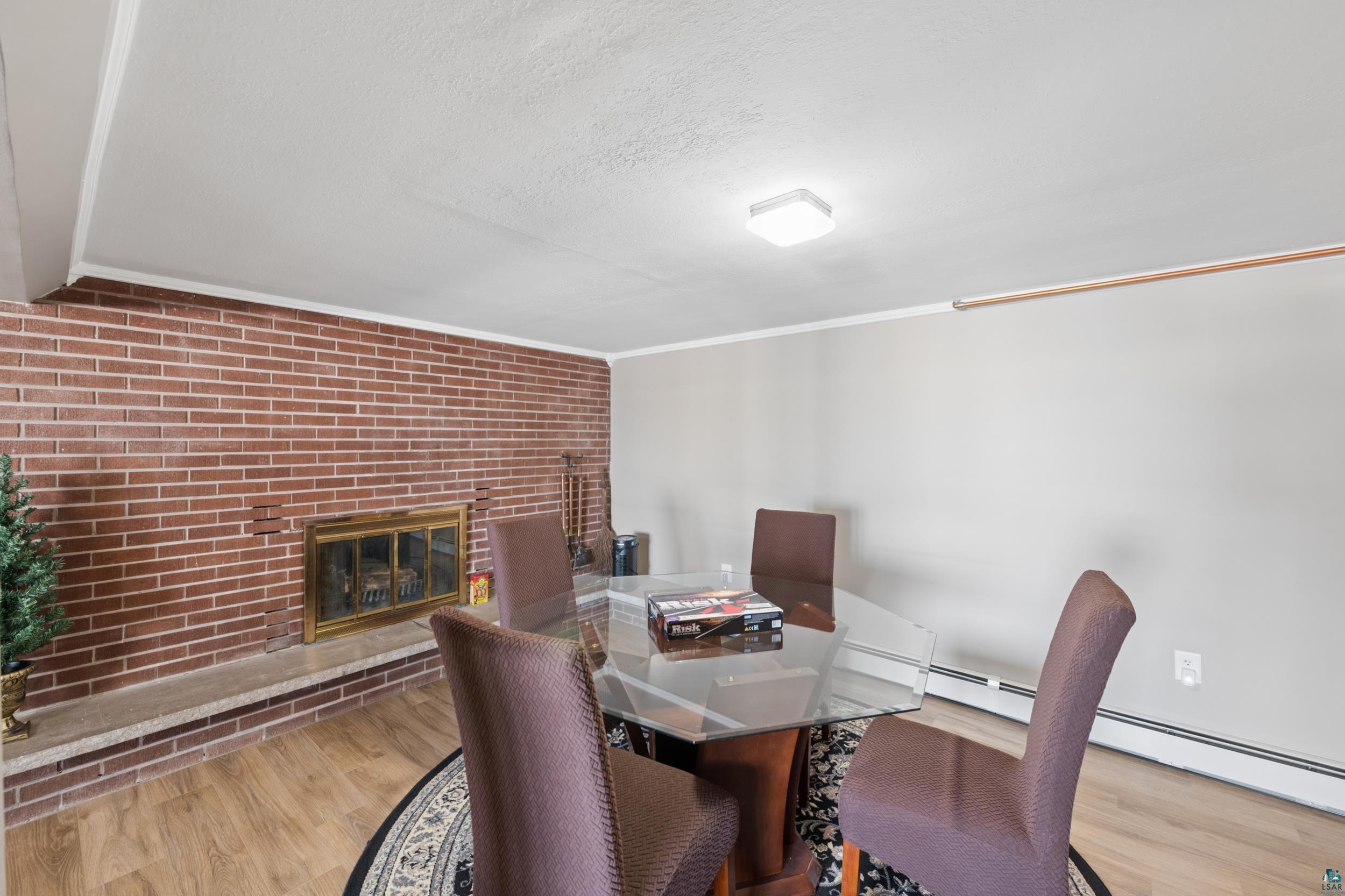 3903 Lake Park Road Ashland, WI 54806 - Photo 31 of 37 Dining area with brick wall, light wood-type flooring, a brick fireplace, crown molding, and a baseboard heating unit