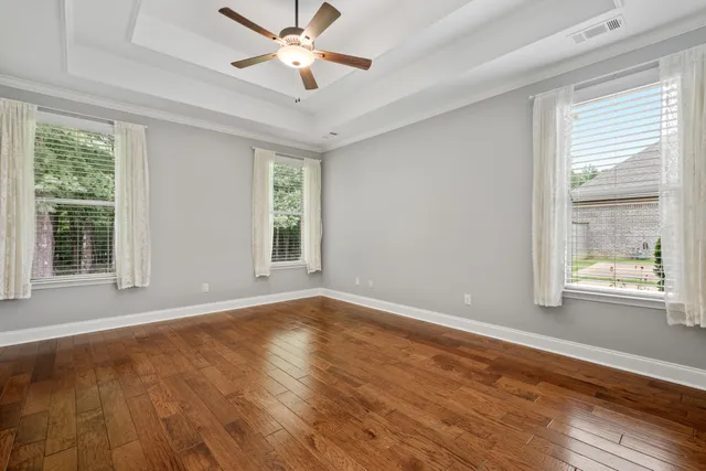 a view of an empty room with wooden floor and a ceiling fan