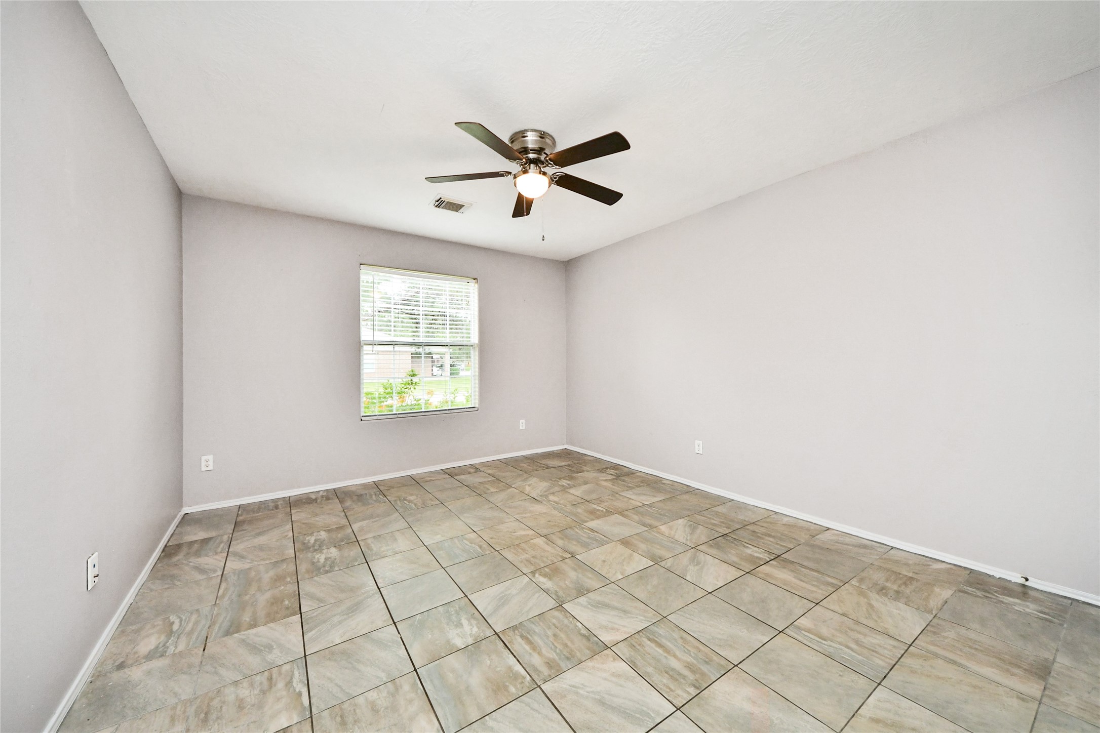 24019 Kingbriar Drive Spring, TX 77373 - Photo 21 of 41 This light-filled bedroom features neutral grey walls, a ceiling fan for comfort, and durable tile flooring, providing a clean and versatile space.