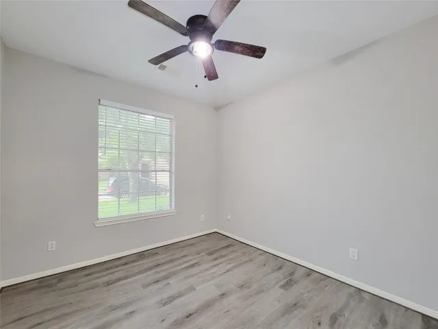 an empty room with wooden floor chandelier fan and windows