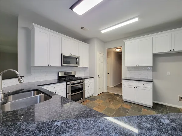 a kitchen with stainless steel appliances granite countertop a sink a stove top oven a counter space and cabinets