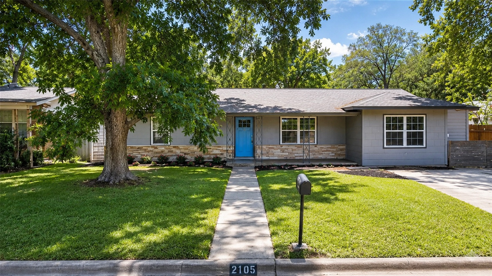 A well-maintained lawn and mature shade trees welcome you to this charming residence with a striking blue door.