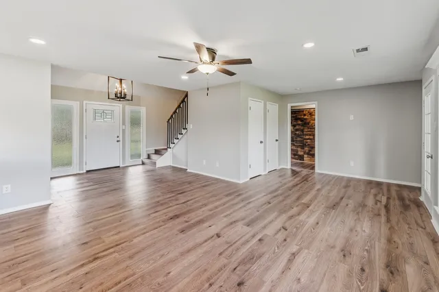 a view of an empty room with wooden floor and a ceiling fan