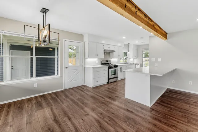 a kitchen with stainless steel appliances granite countertop a refrigerator a sink dishwasher a stove and white countertops with wooden floor