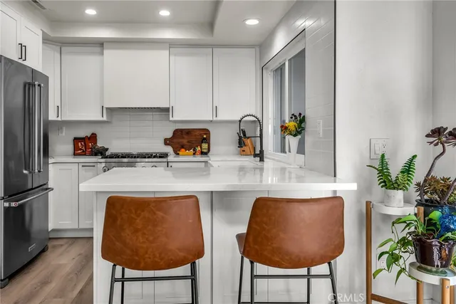 a kitchen with stainless steel appliances granite countertop a refrigerator a stove a sink and white cabinets with wooden floor