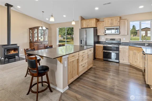 a open kitchen with stainless steel appliances granite countertop a stove top oven a sink dishwasher a dining table and chairs with wooden floor