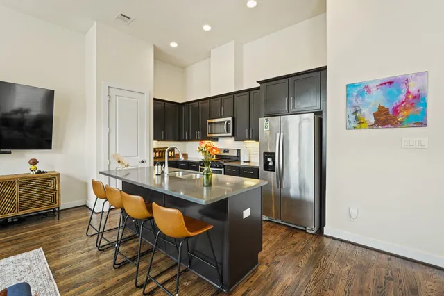 a kitchen with stainless steel appliances granite countertop a refrigerator a stove a sink a dining table and chairs with wooden floor