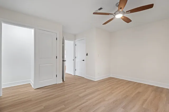 an empty room with wooden floor fan and windows