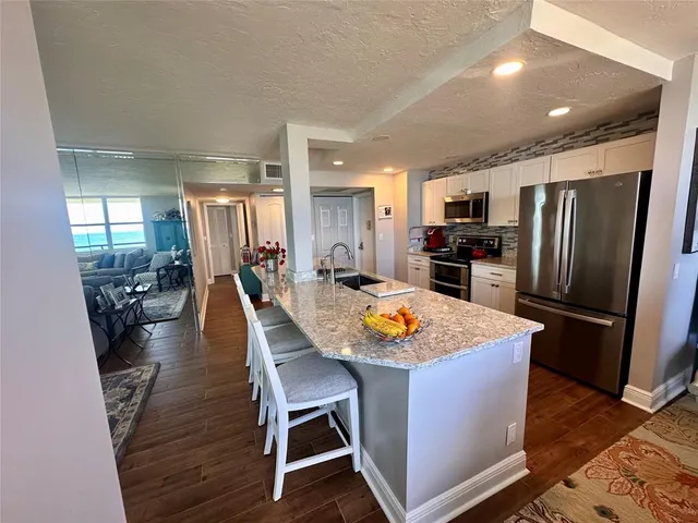 a kitchen with stainless steel appliances granite countertop a refrigerator a stove top oven a sink dishwasher and white cabinets with wooden floor