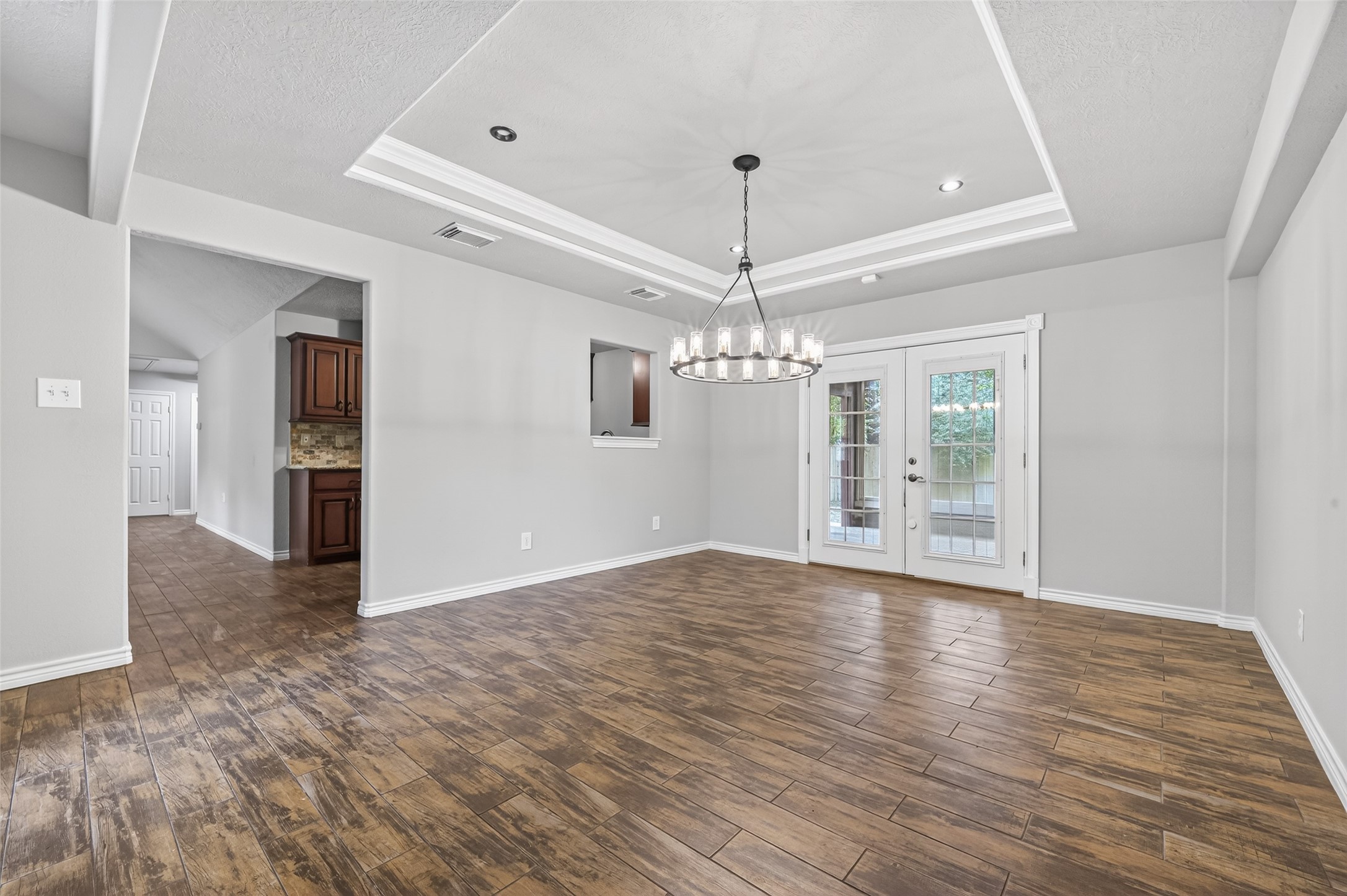 1007 West Cedar River Road Conroe, TX 77316 - Photo 18 of 48 This spacious dining area features elegant wood-like tile flooring, a modern chandelier, and double glass doors leading to the outside. The room has a stylish tray ceiling and is adjacent to the kitchen, offering a cozy yet sophisticated atmosphere.