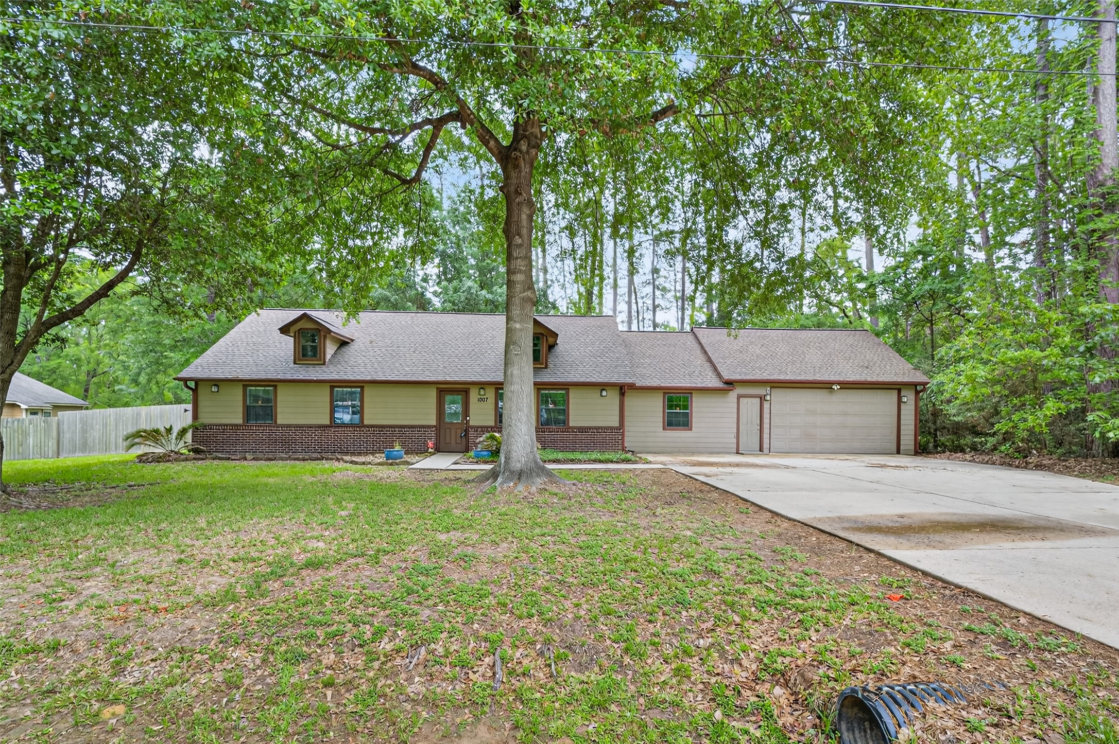 1007 West Cedar River Road Conroe, TX 77316 - Photo 2 of 48 Charming single-story home with a brick and siding exterior, nestled among mature trees. Features a spacious driveway leading to a two-car garage. The front yard is expansive, offering plenty of greenery and shade. The home is on Lot 10 & 11.