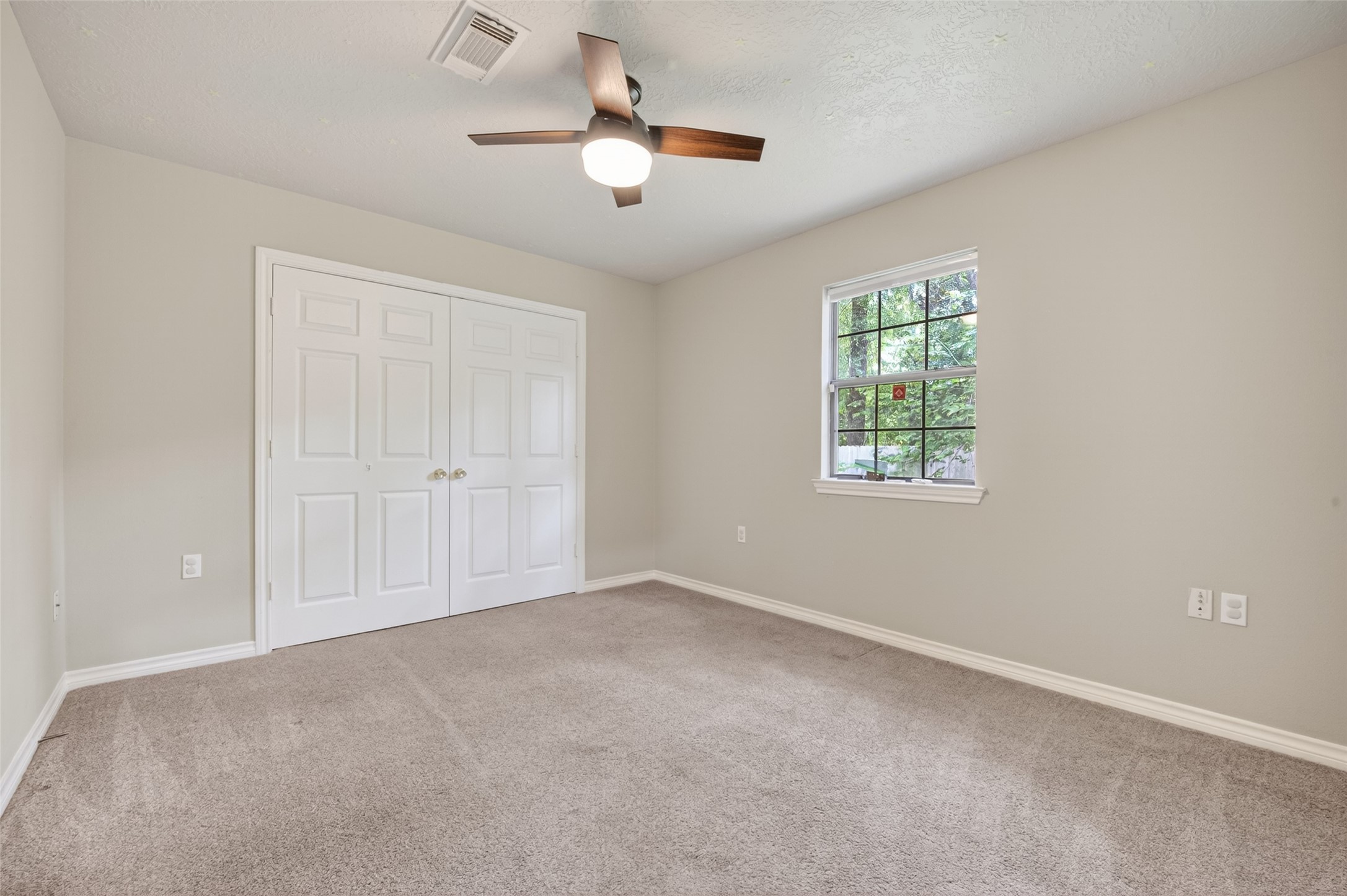 1007 West Cedar River Road Conroe, TX 77316 - Photo 21 of 48 This bedroom features carpeting, neutral walls, a ceiling fan, and a double-door closet. A window provides natural light and a view of the greenery outside. #2 secondary bedroom.