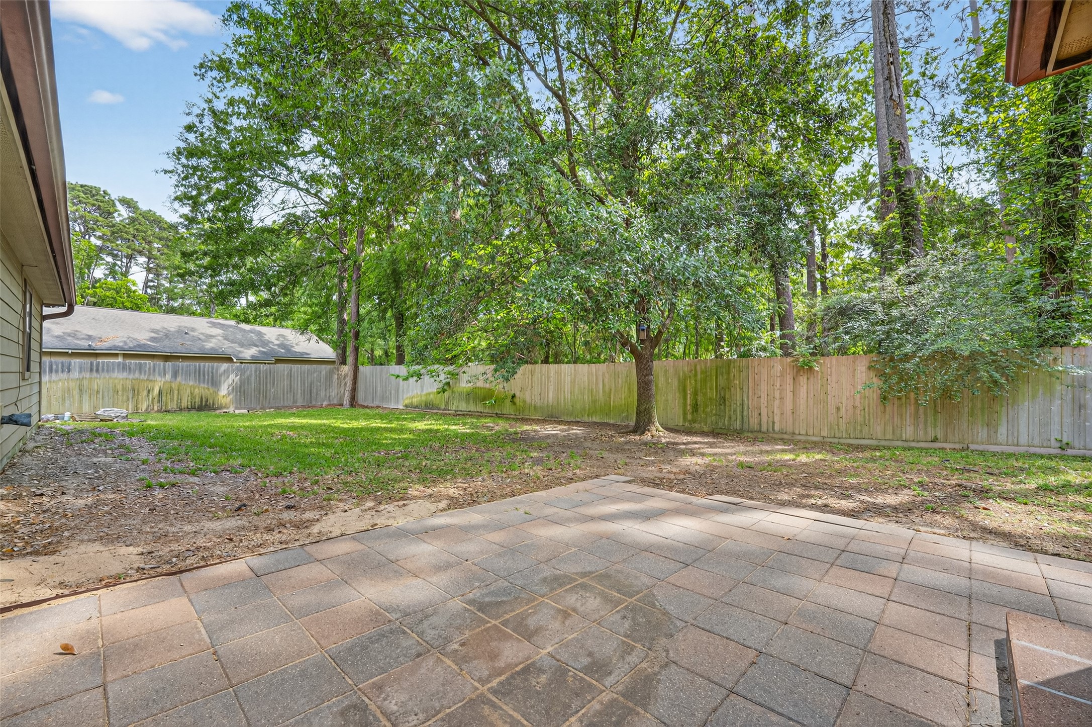 1007 West Cedar River Road Conroe, TX 77316 - Photo 37 of 48 Spacious backyard featuring a paved patio area, lush greenery, and mature trees, all enclosed by a wooden fence for privacy. Ideal for outdoor entertaining and relaxation.