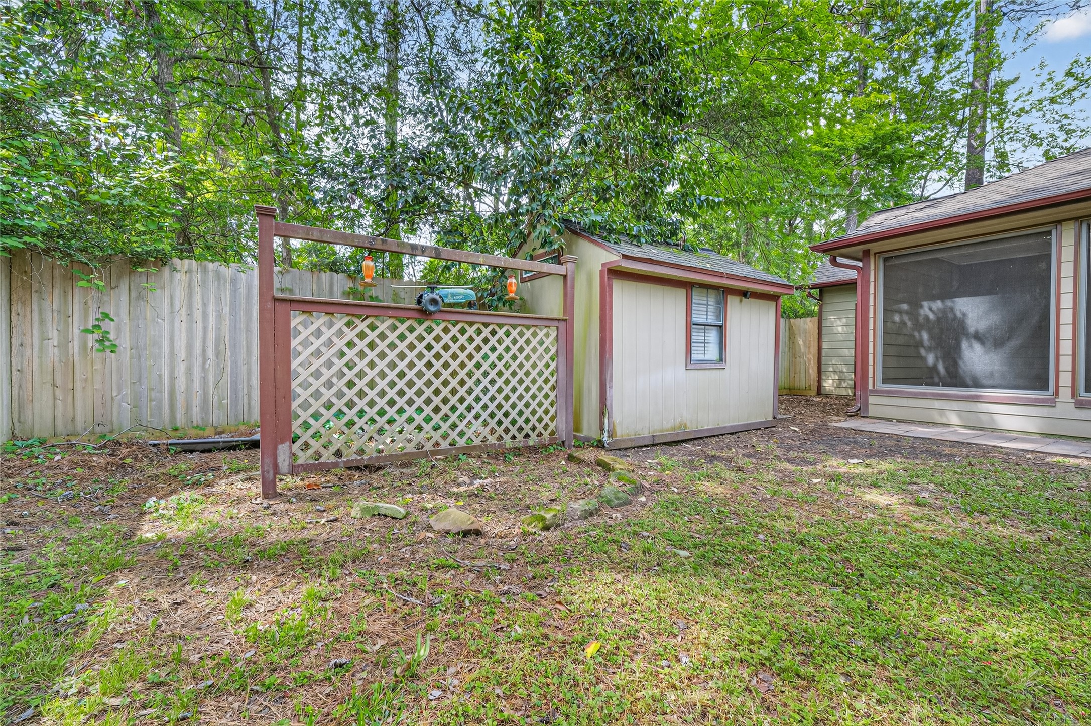 1007 West Cedar River Road Conroe, TX 77316 - Photo 40 of 48 This backyard features a small storage shed, lattice fence, and a screened-in porch, surrounded by lush greenery for added privacy.