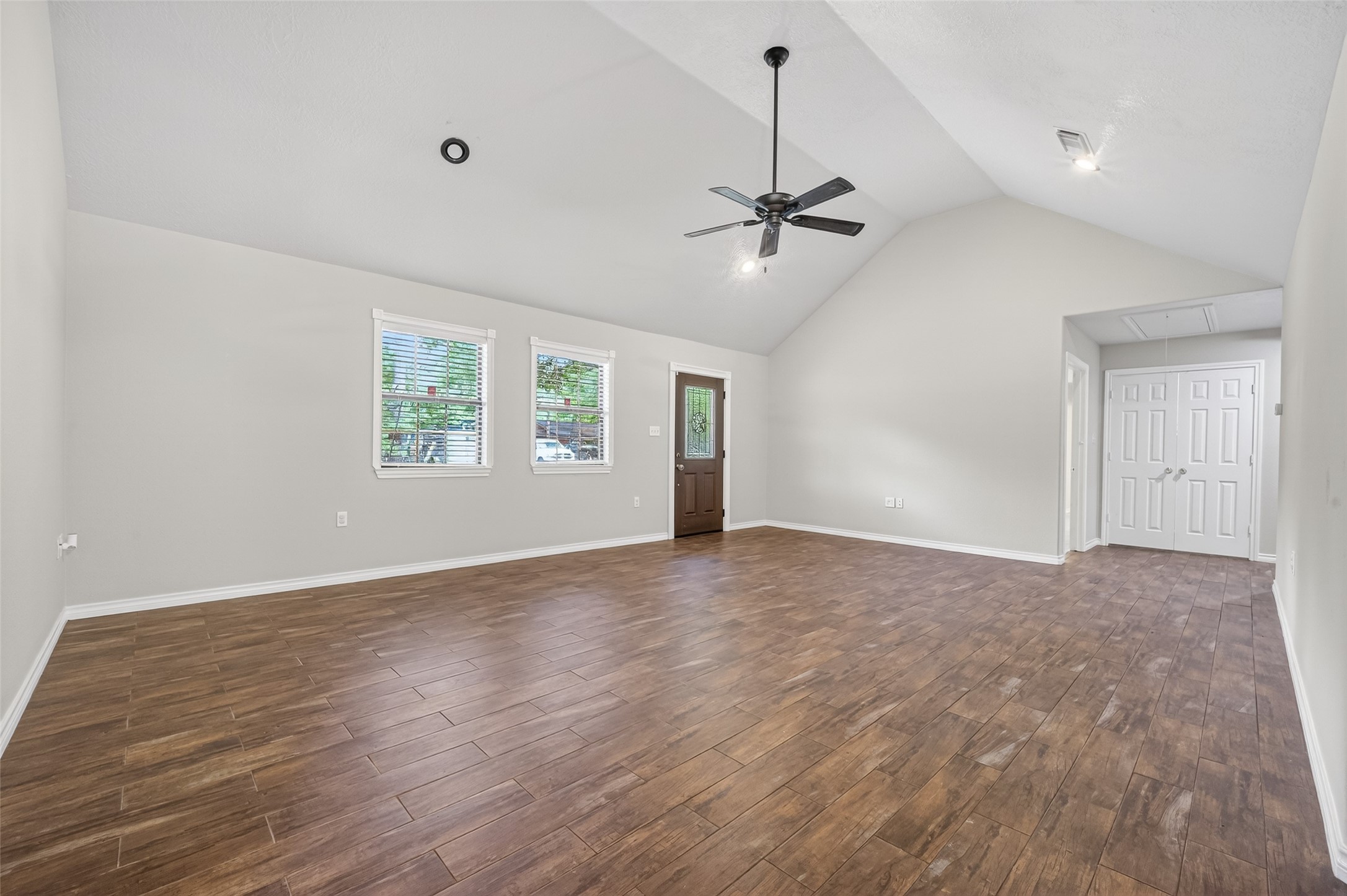 1007 West Cedar River Road Conroe, TX 77316 - Photo 7 of 48 This spacious living room features high vaulted ceilings, wood-look tile flooring, and ample natural light from two large windows. It includes a ceiling fan and a stylish entry door, offering a modern and inviting space.