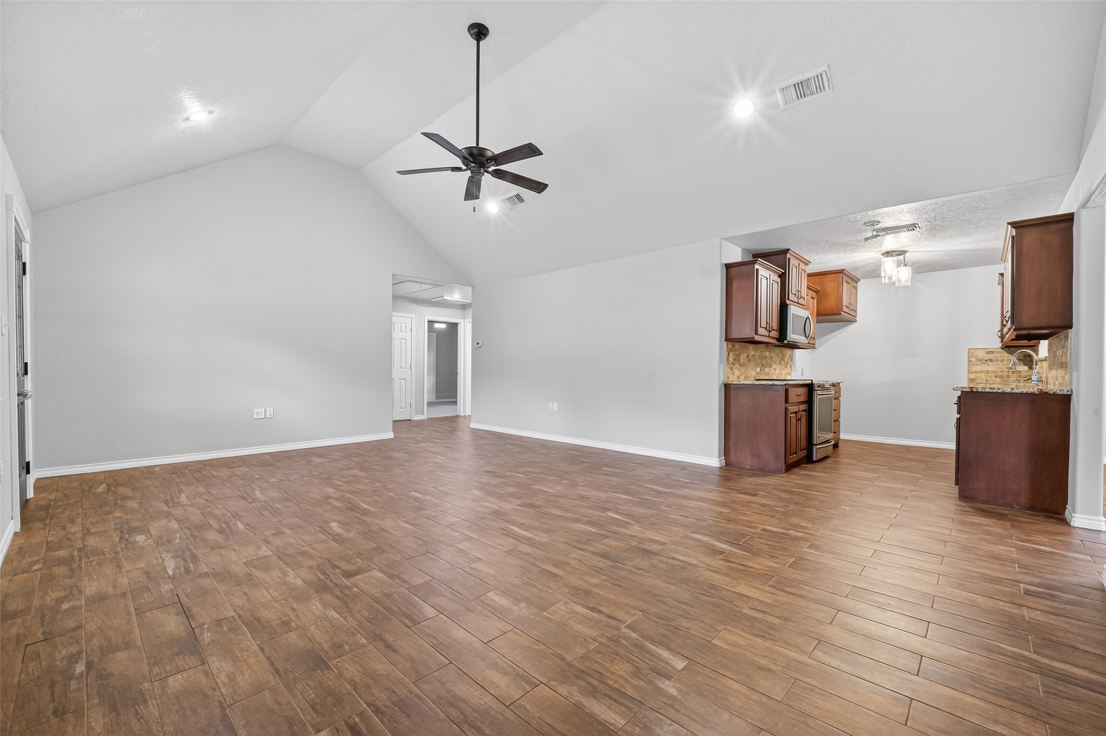 1007 West Cedar River Road Conroe, TX 77316 - Photo 9 of 48 This photo showcases a spacious open-plan living area with vaulted ceilings and wood-look flooring. The kitchen features dark wood cabinets, stainless steel appliances, and a tile backsplash, offering a modern and inviting atmosphere.