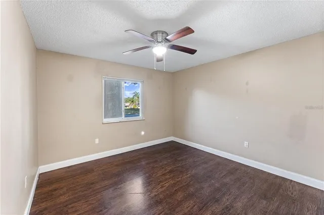 an empty room with wooden floor ceiling fan and window