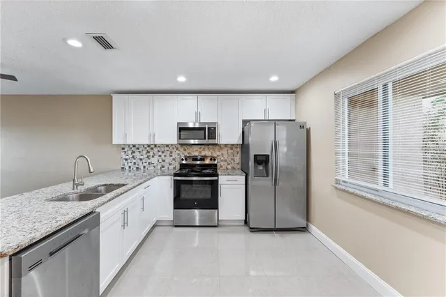 a kitchen with stainless steel appliances granite countertop a sink a stove a refrigerator cabinets and a window