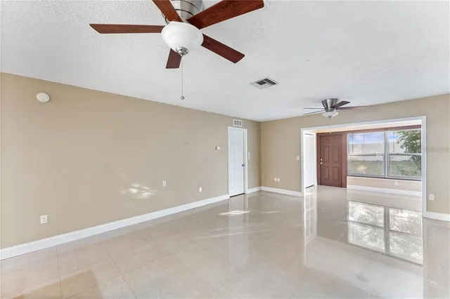 an empty room with chandelier fan and windows
