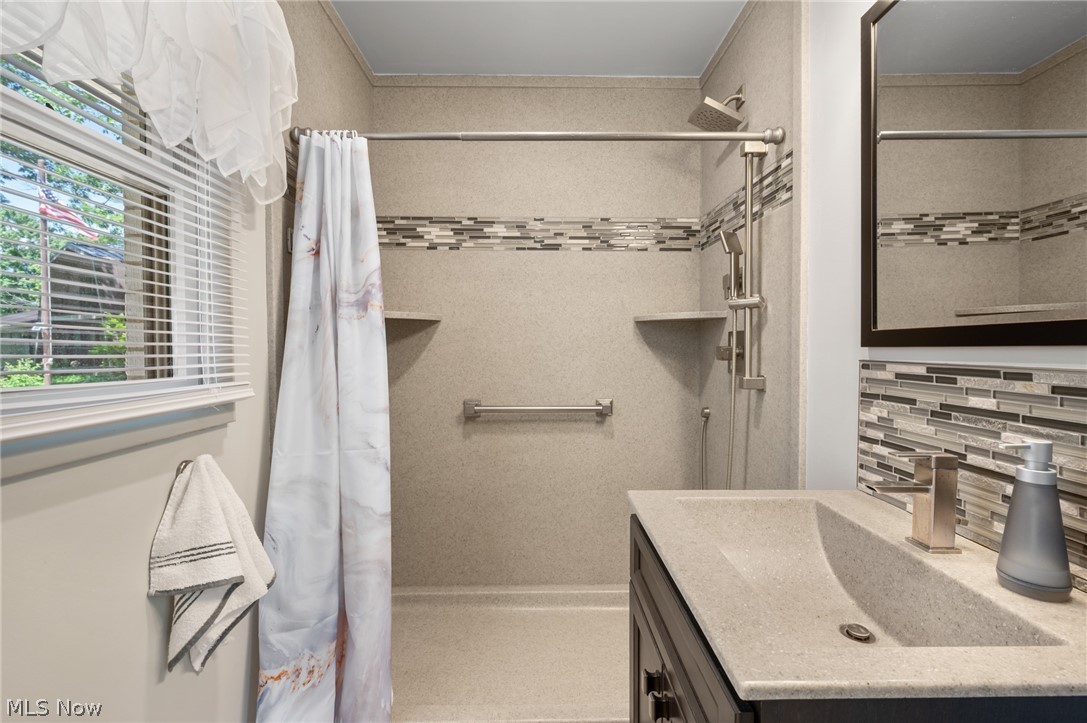 685 Sunnyside Road Vermilion, OH 44089 - Photo 22 of 50 Bathroom featuring a walk-in shower with a decorative tile band, a vanity with an integrated sink, a dark wood-finish cabinet, and a framed mirror