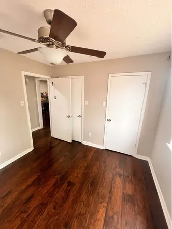 an empty room with wooden floor closet fan and windows