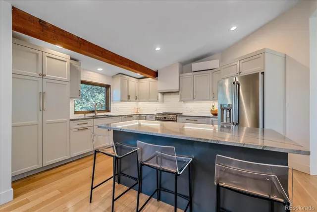 a kitchen with stainless steel appliances kitchen island granite countertop a refrigerator a stove a sink dishwasher and a dining table with wooden floor