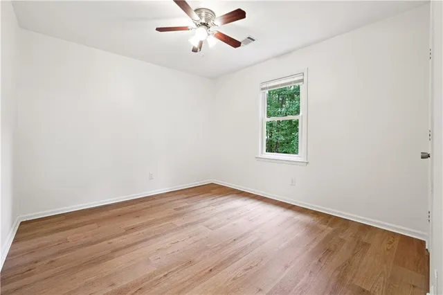 an empty room with wooden floor chandelier fan and windows
