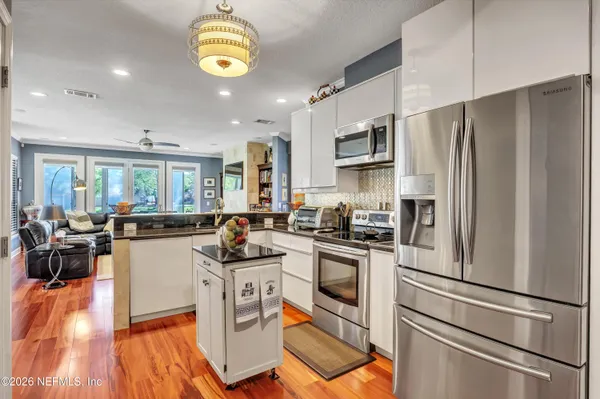 a kitchen with stainless steel appliances granite countertop a refrigerator a stove top oven a sink dishwasher and white cabinets with wooden floor
