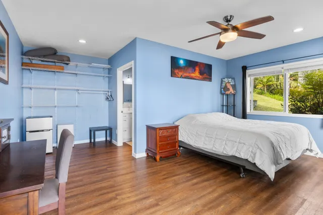 a bedroom with a bed a chair and a potted plant with wooden floor