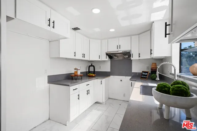 a kitchen with granite countertop a sink white cabinets and stainless steel appliances