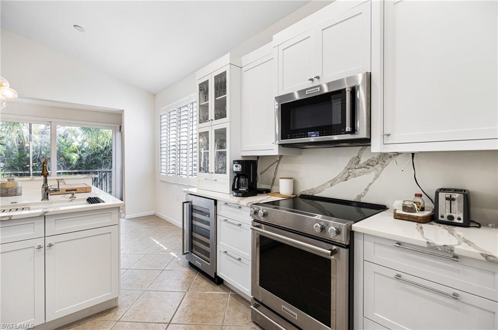 19071 Ridgepoint Drive, Unit 202 Estero, FL 33928 - Photo 9 of 26 Kitchen with appliances with stainless steel finishes, white cabinetry, light tile patterned flooring, wine cooler, and lofted ceiling