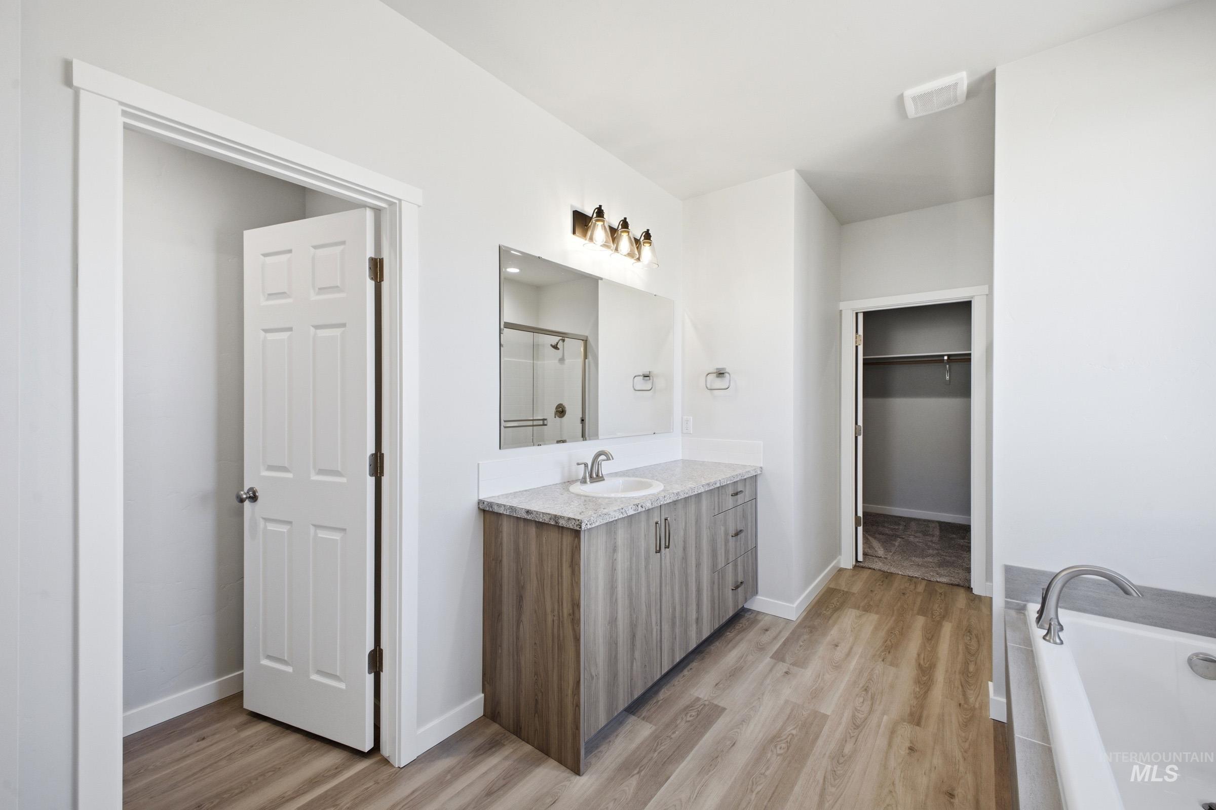 13633 Redway Court Caldwell, ID 83607 - Photo 25 of 29 Bathroom featuring vanity, light wood-style floors, a bath, a walk in closet, and a stall shower