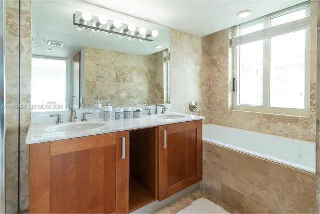 a bathroom with a granite countertop sink a large mirror a bathtub and next to a window