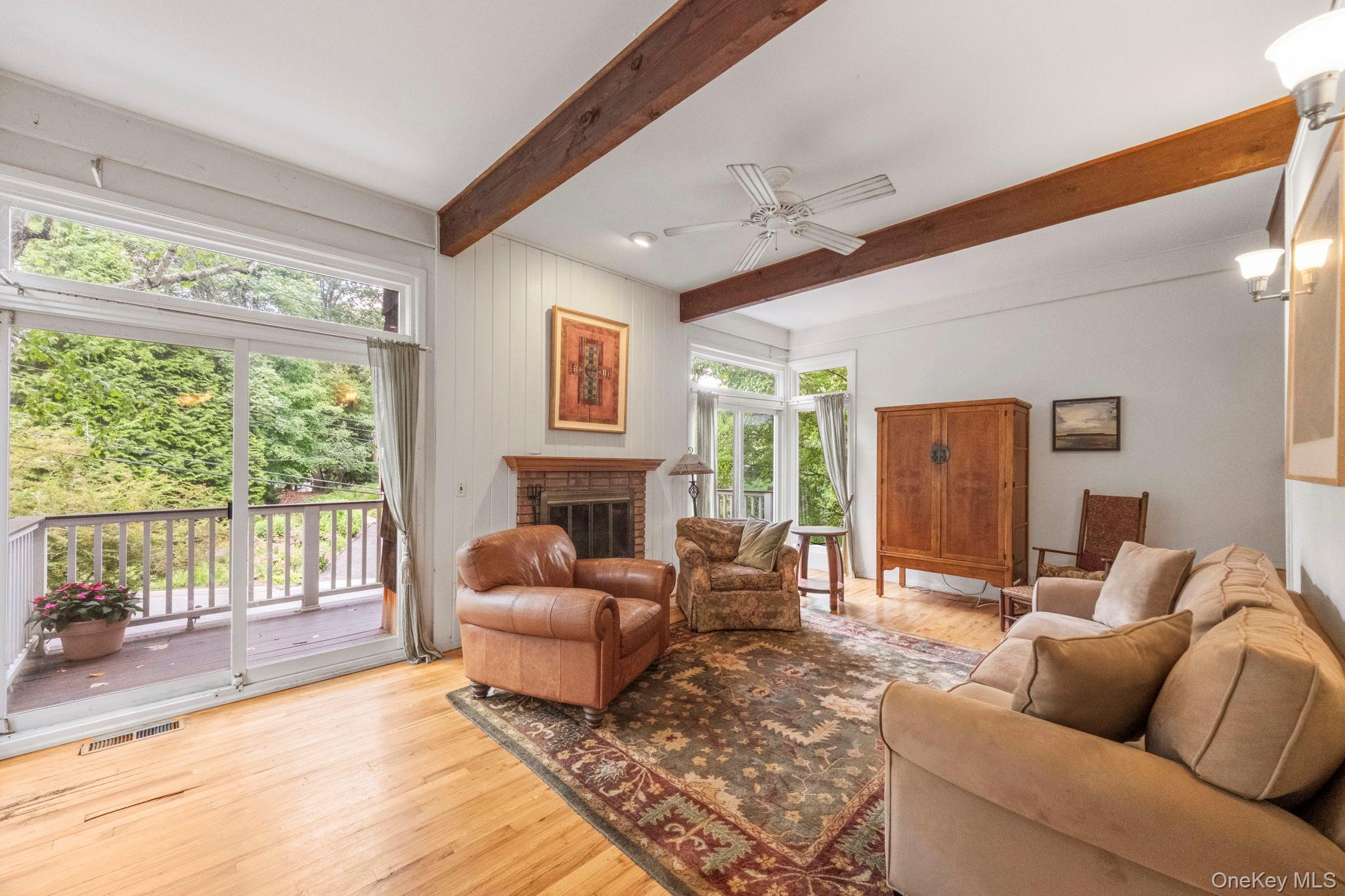 73 Bramblebrook Road Ardsley, NY 10502 - Photo 4 of 35 Spacious living area featuring exposed wood beams, a brick fireplace with a wood mantle, wood-finish flooring, and sliding glass doors opening to a deck