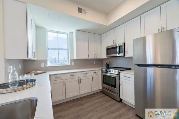 a kitchen with stainless steel appliances granite countertop a refrigerator a stove a sink and white cabinets with wooden floor