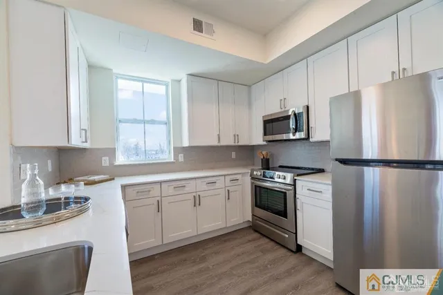 a kitchen with stainless steel appliances granite countertop a refrigerator a stove a sink and white cabinets with wooden floor