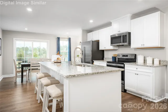 a kitchen with stainless steel appliances granite countertop a stove a sink a microwave a refrigerator and white cabinets with wooden floor