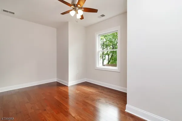 an empty room with wooden floor chandelier fan and windows