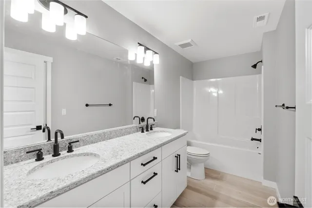 a bathroom with a granite countertop sink a toilet a mirror and shower