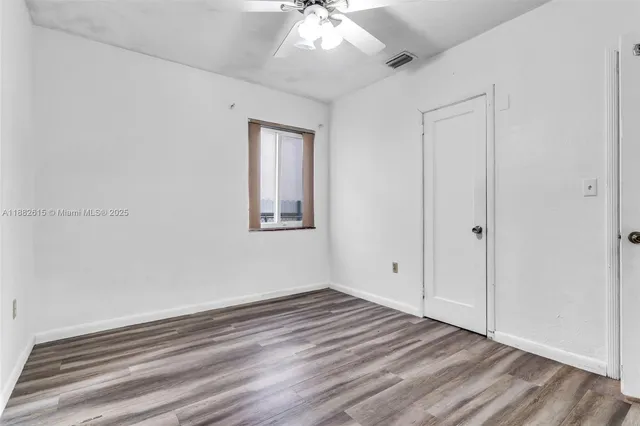 an empty room with wooden floor chandelier fan and windows