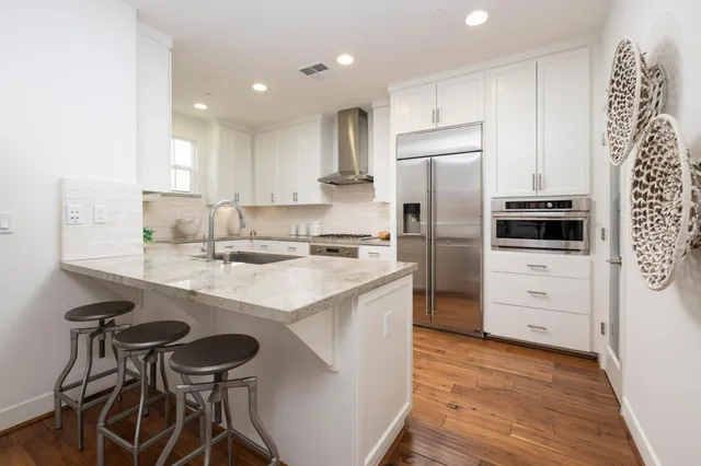 a kitchen with white cabinets stainless steel appliances a sink and wooden floor
