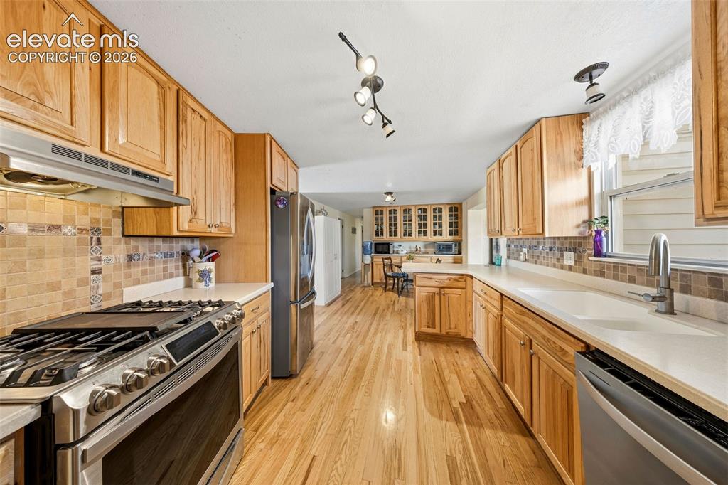 13075 Blaney Road South Peyton, CO 80831 - Photo 7 of 40 Expansive kitchen featuring custom wood cabinets, flooring, light wood cabinetry, light-toned countertops, a tile backsplash, and new stainless steel appliances