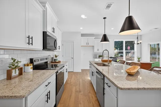a kitchen with stainless steel appliances kitchen island granite countertop a stove a refrigerator a kitchen island a dining table and chairs with wooden floor