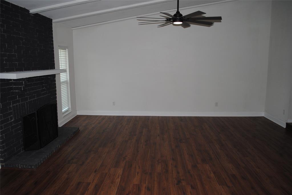 5241 Reed Drive The Colony, TX 75056 - Photo 7 of 26 Spacious room featuring wood-finish flooring, a painted brick fireplace with a white mantel, and a multi-blade ceiling fan