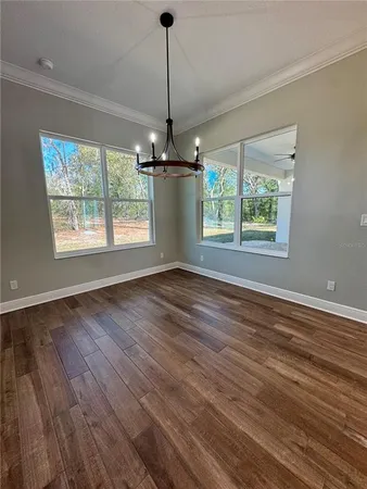 a view of an empty room with wooden floor chandeliers and a window