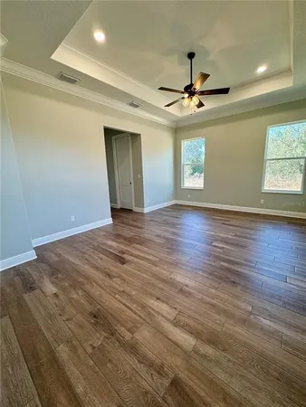 an empty room with wooden floor ceiling fan and windows